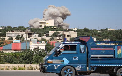 A truck drives as a plume of smoke rises from a building during a reported Russian airstrike on Syria's northwestern rebel-held Idlib province, on June 25, 2023. (Abdulaziz KETAZ / AFP)