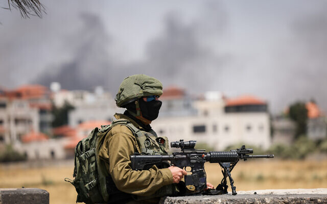 Israeli soldiers at the entrance to Turmus Ayya, as smoke rises over the West Bank town after settlers set fire to cars and homes, June 21, 2023. (Yonatan Sindel/ Flash90)